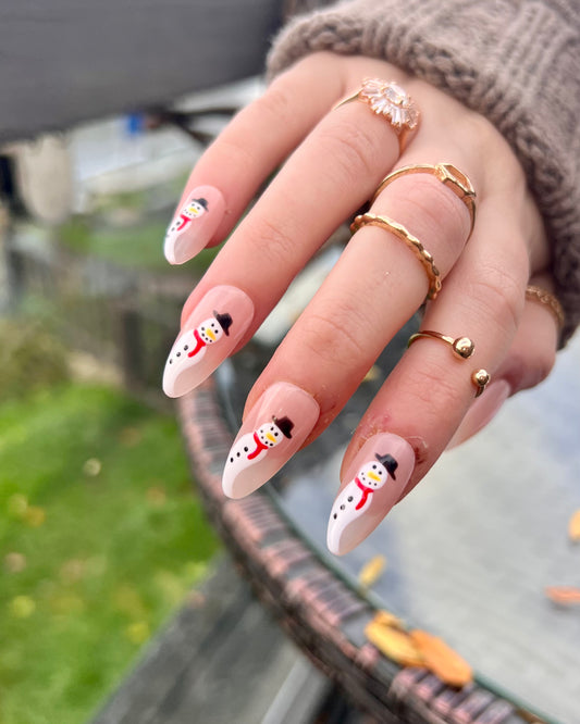 Almond press on nails; subtle nude christmas nails with little snowmen on each nail with red scarves.