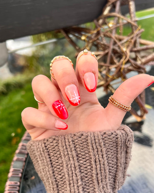 Short almond press on nails with bright red french tip nails and little snowflake details on the middle and ring finger.