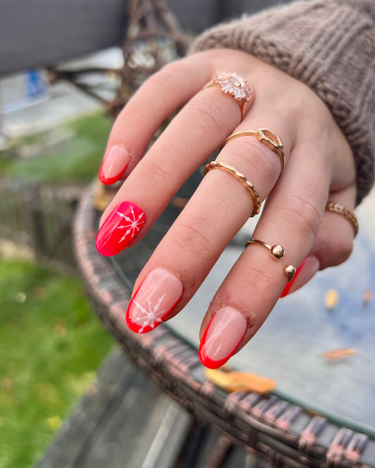 Cute natural short almond press on nails for christmas and winter. French tips in bright red with little snowflakes.